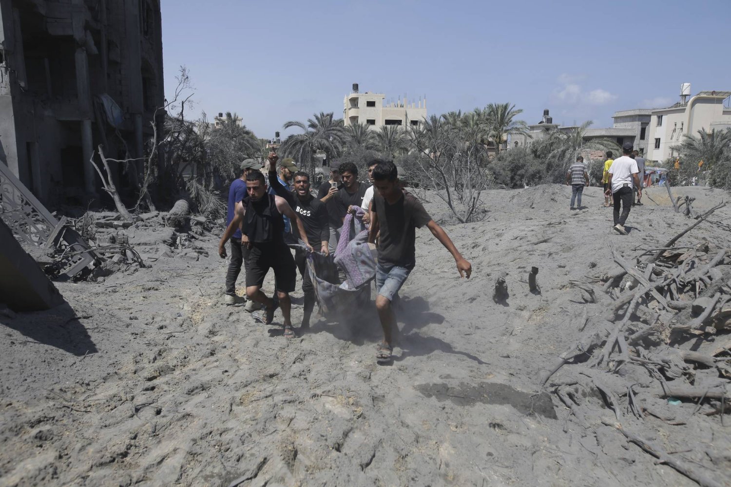 فلسطينيون يحملون جثمان أحد القتلى من موقع القصف إسرائيلي بمنطقة المواصي في خان يونس أمس (أ.ب)