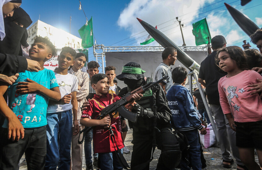 أطفال فلسطينيون يحيطون بأحد عناصر القسام وطفل يعاين سلاحا رشاشا خلال عرض عسكري للمقاومة الفلسطينية في مدينة غزة. / Globallookpress