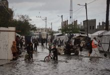 فلسطينيون يسيرون في شارع غمرته المياه بجوار مخيم مؤقت بعد هطول أمطار غزيرة في دير البلح وسط قطاع غزة، الثلاثاء 25 نوفمبر الماضي / AP